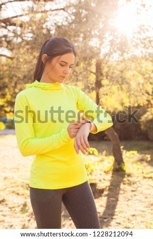Sports lifestyle, autumn. Beautiful, young girl in sportswear looking fitness tracker, smart watch after jogging, playing sports in the park, forest