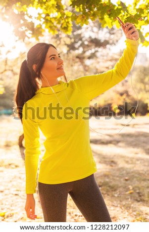 Beautiful young girl in sportswear takes a selfie on the phone and listens to music while jogging in the forest, park in the fall at sunset. Sports lifestyle, autumn