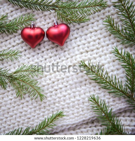 Warm winter picture with a frame of green Christmas tree branches and two red hearts on a white knitted background