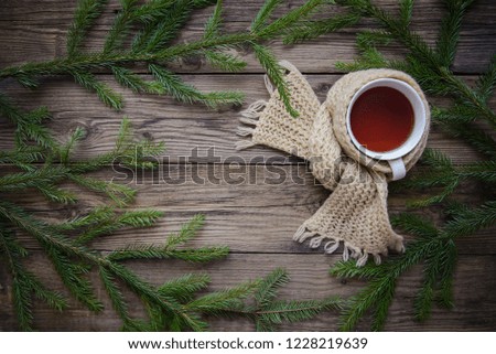 Beautiful cozy Christmas picture with a mug of hot tea in a scarf with fir branches on a wooden background