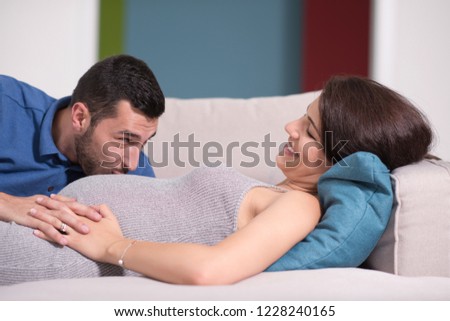 Happy future dad listening the belly of his pregnant wife while relaxing on sofa at home
