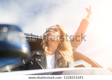 Photo of young woman with glasses popping out of black car