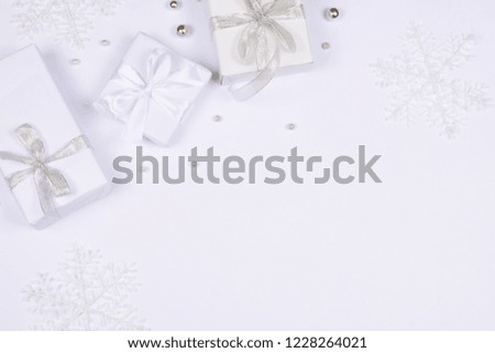 Three elegant white gift boxes tied up with silver and silk ribbons on the background of the same tone decorated with shiny beads and big snowflakes. Flat lay with copy space.