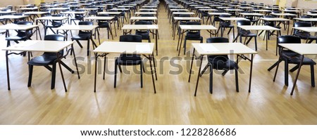 View of large exam room hall and examination desks tables lined up in rows ready for students at a high school to come and sit their exams tests papers.  Royalty-Free Stock Photo #1228286686