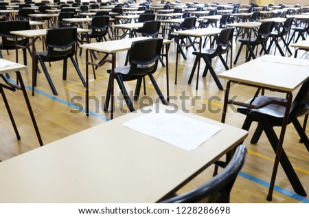 View of large exam room hall and examination desks tables lined up in rows ready for students at a high school to come and sit their exams tests papers.  Royalty-Free Stock Photo #1228286698