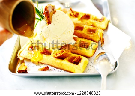 Pouring honey from wood cup into waffle top with vanilla ice cream decorate with crunchy toffee caramel on white isolated table, happy Hanukkah day festival for light candles celebrate