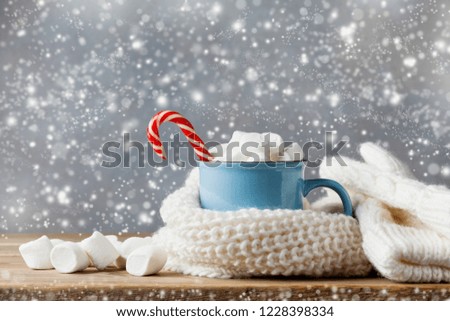Winter lifestyle with cup of hot cocoa with marshmallows and knitted scarf on wooden background. Snow effect.
