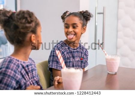 Play tricks. Funny dark-haired girl with nice hairstyle showing tongue while playing tricks with sibling