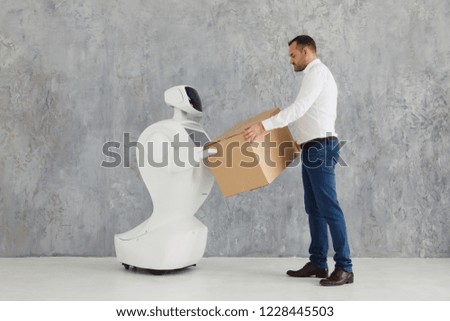Modern Robotic Technologies. A man communicates with a robot, with cardboard box in hand. delivery concept.