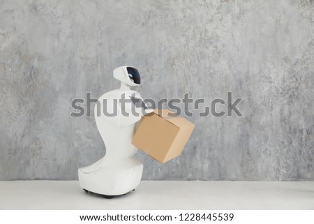 Humanoid autonomous robot with cardboard box in hand on grey background. the robot delivers the parcel. delivery concept.