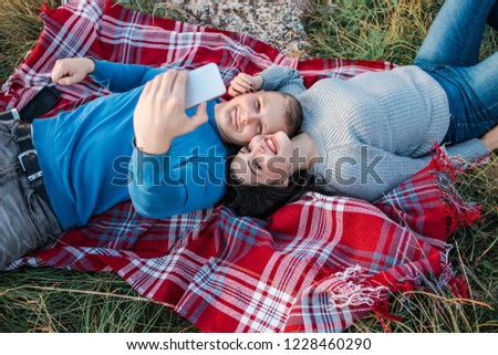 Happy young couple making selfie near coast of Black Sea. They laying on the plaid and smiling. Concept of freedom, love and travelling.
