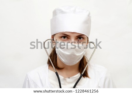 a woman in a white robe, mask and black gloves, holding a stethoscope to listen to the patient's heartbeat