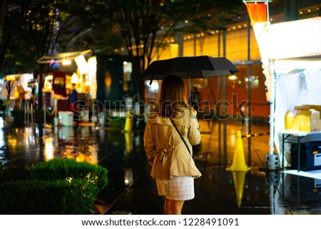 A woman is walking alone at the night street in the rainy season.