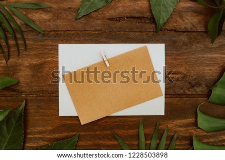 mock-up with blank paper card and green leaves on wooden background Empty space. Styled stock photo, web banner. Flat lay, top view.