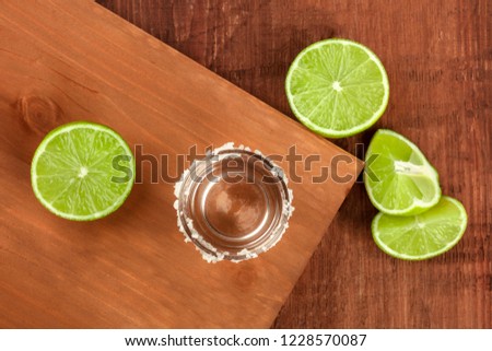 A tequila shot with lime wedges, shot from the top on dark rustic textures with copy space