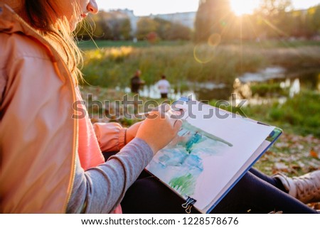 Teenager school girl drawing beautiful picture outdoor in the park at sunset. Open air activity for school age children concept. Close up
