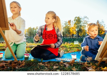 Three different age children painting pictures outdoor in autumn park at sunset. Open air creative activity for school age children concept.