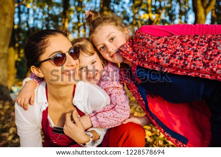 Cute two little daughter playing on a piggy back ride with their mother. Female teacher play with girl child outdoor. Open air activity for preschool age children concept.