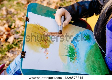 Teenager school girl drawing beautiful picture outdoor in the park. Open air activity for school age children concept. Close up