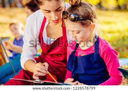 Young female teacher and happy girl are painting outdoor in the park. The concept of a happy family.