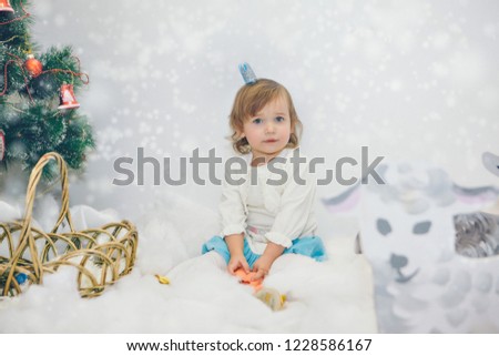 a little girl celebrates the new year: a child among the snow of cotton wool, painted sheep, Christmas tree and stars