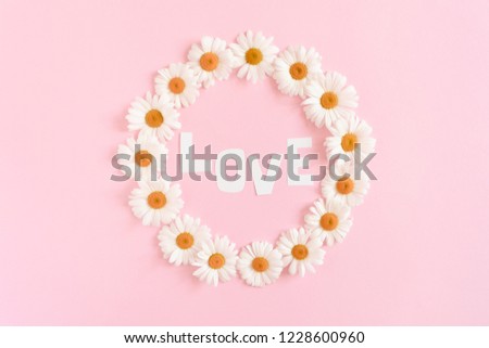Word Love made of letters cut out of paper. Wreath made of white chamomile on a pink pastel background