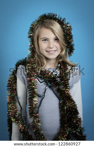 Girl wrapped in Christmas decorations isolated on blue.