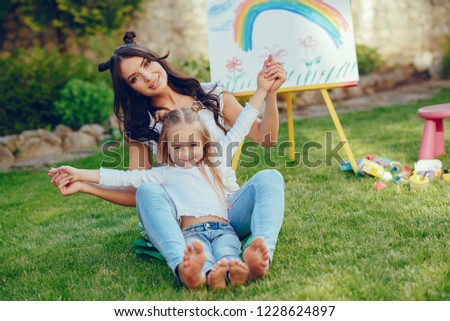 Beauty mother paint with her little daughter. Stylish woman drawing the picture with little girl. Cute kid in a white t-shirt and blue jeans