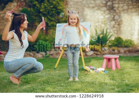 Beauty mother paint with her little daughter. Stylish woman drawing the picture with little girl. Cute kid in a white t-shirt and blue jeans