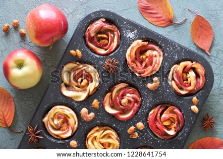Tray of apple roses baked in puff pastry on gray textured background with Autumn leaves and red apples