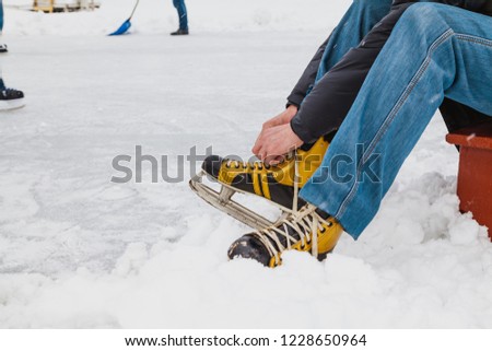 Hands tie a long string on the yellow leather boot of the modern skate. Around is loose snow
