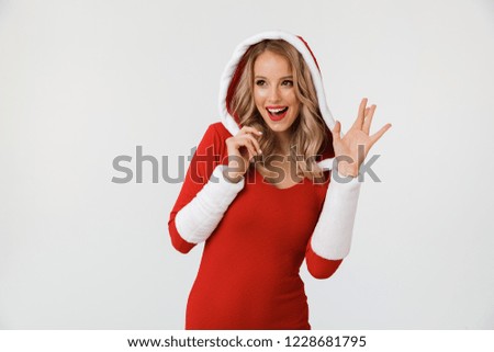 Portrait of a joyful blonde woman dressed in red New Year costume standing isolated over white background, waving