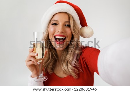 Portrait of a laughing blonde woman dressed in red New Year costume standing isolated over white background, holding glass of champagne, celebrating, taking a selfie