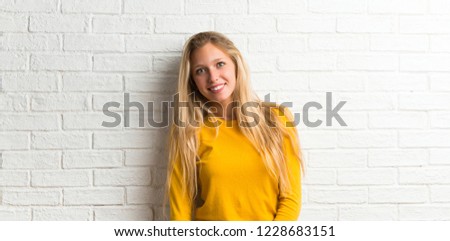 Happy blonde young girl on white brick wall background