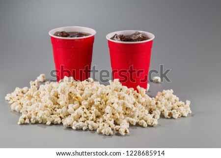 Closeup popcorn on the background of red plastic cups with fizzy drink. Winter picture with snow.