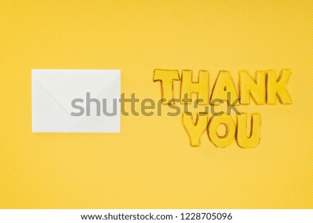 thank you lettering in cookies with blank white envelope isolated on yellow background