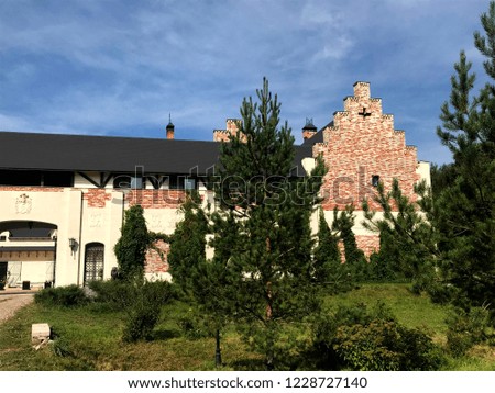 Old castle building made of bricks, standing near to forest, with big territory and heraldic signs on the walls on the summer day. Arched entrance to the courtyard of the castle