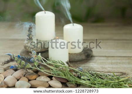 Three candles with smoke on river pebbles with lavender on wooden table and herbal background