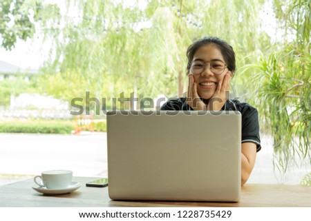 Asian woman student working on laptop with earphone looking at camera.
