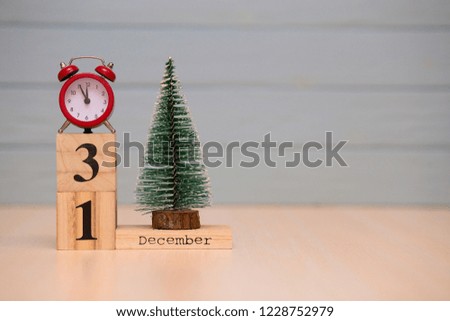 December 31st set on wooden calendar with new year tree and red alarm clock on blue background. Clock show five minutes to midnight