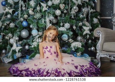Beautiful little girl sitting on the floor near the Christmas tree / copy space