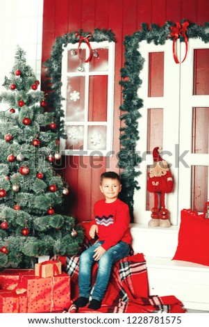 Boy is smiling and sitting on the chair near beautiful Christmas tree.  New Year Celebration. Decorations.  Xmas event