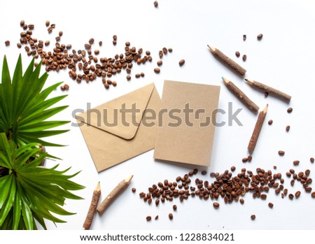 Wooden color pencils and green plant, card with envelope mockup and coffee beans on a white background; top view, flat lay; overhead view