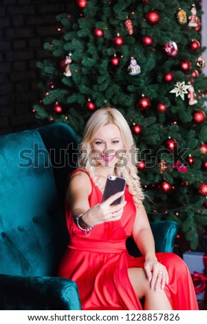 Vertical portrait of beauty young woman taking selfie near holiday Christmas tree using digital front camera of modern smartphone. Vertical color photography.