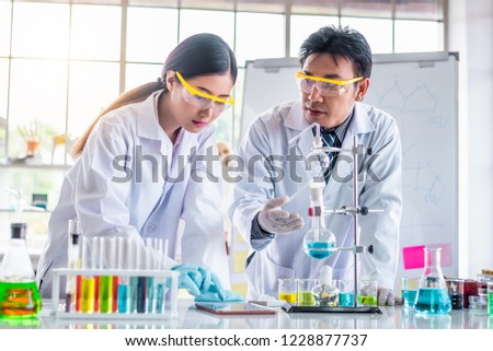 Attractive scientist looking chemical sample in flask at laboratory with lab glassware background. Science or chemistry research and development concept.