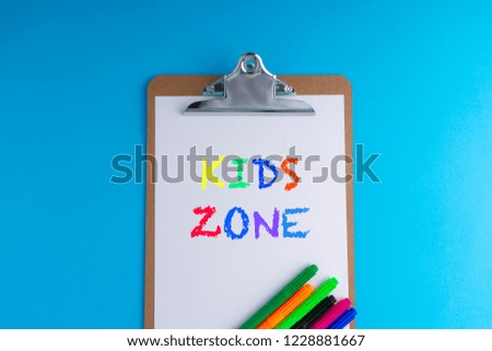 Clipboard and words KIDS ZONE on blue background with selective focus and crop fragment