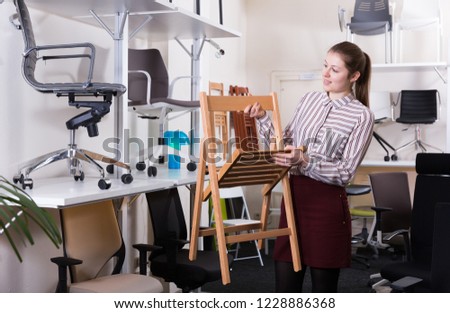 Young woman choosing stylish chairs for apartment in salon of furniture