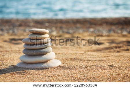 Zen pyramid of spa stones on the blurred sea background. Sand on a beach. Sea shores. Water waves texture. Left side of photo. Place for text. 