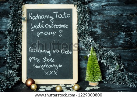 on a Christmas background a blackboard with a message in polish language from child to father: Drive carefully, we are waiting at Christmas table for you
