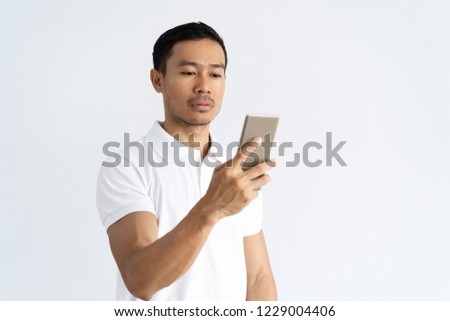 Focused serious guy texting message. Young mix raced man dressed in white using smartphone. Communication or wireless connection concept